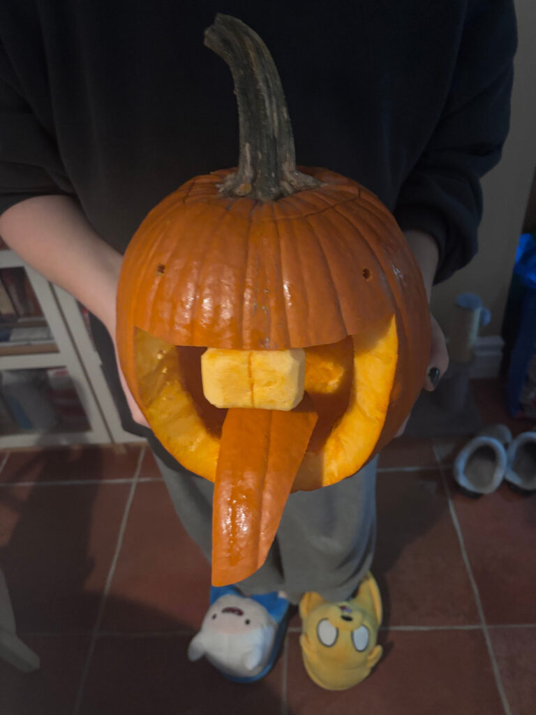 A pumpkin which has been carved to have two tiny eyes and a huge pair of buck teeth with an outstretched tongue and gaping mouth